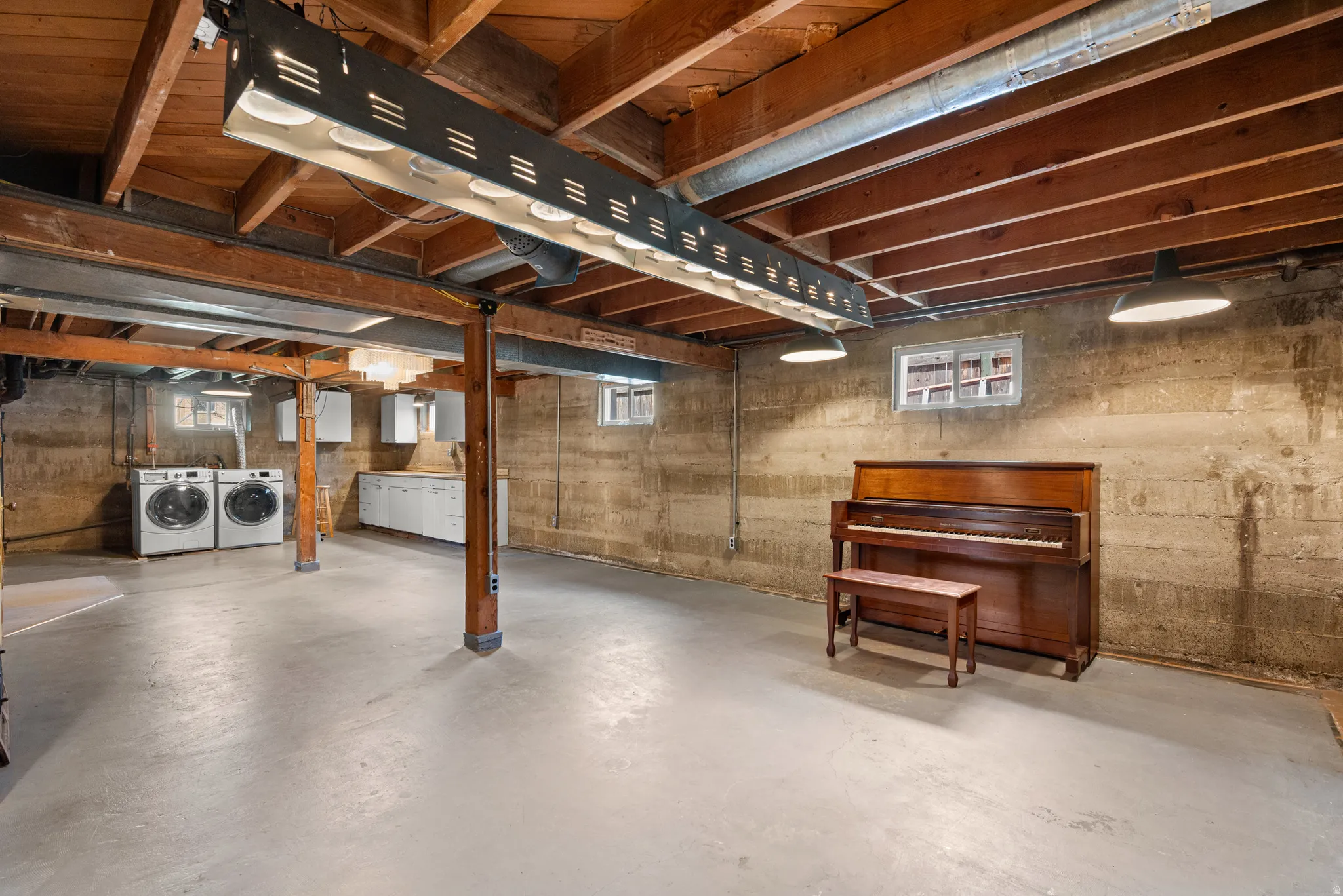 Spacious unfinished basement featuring exposed wood joists, concrete flooring, and multiple utility windows