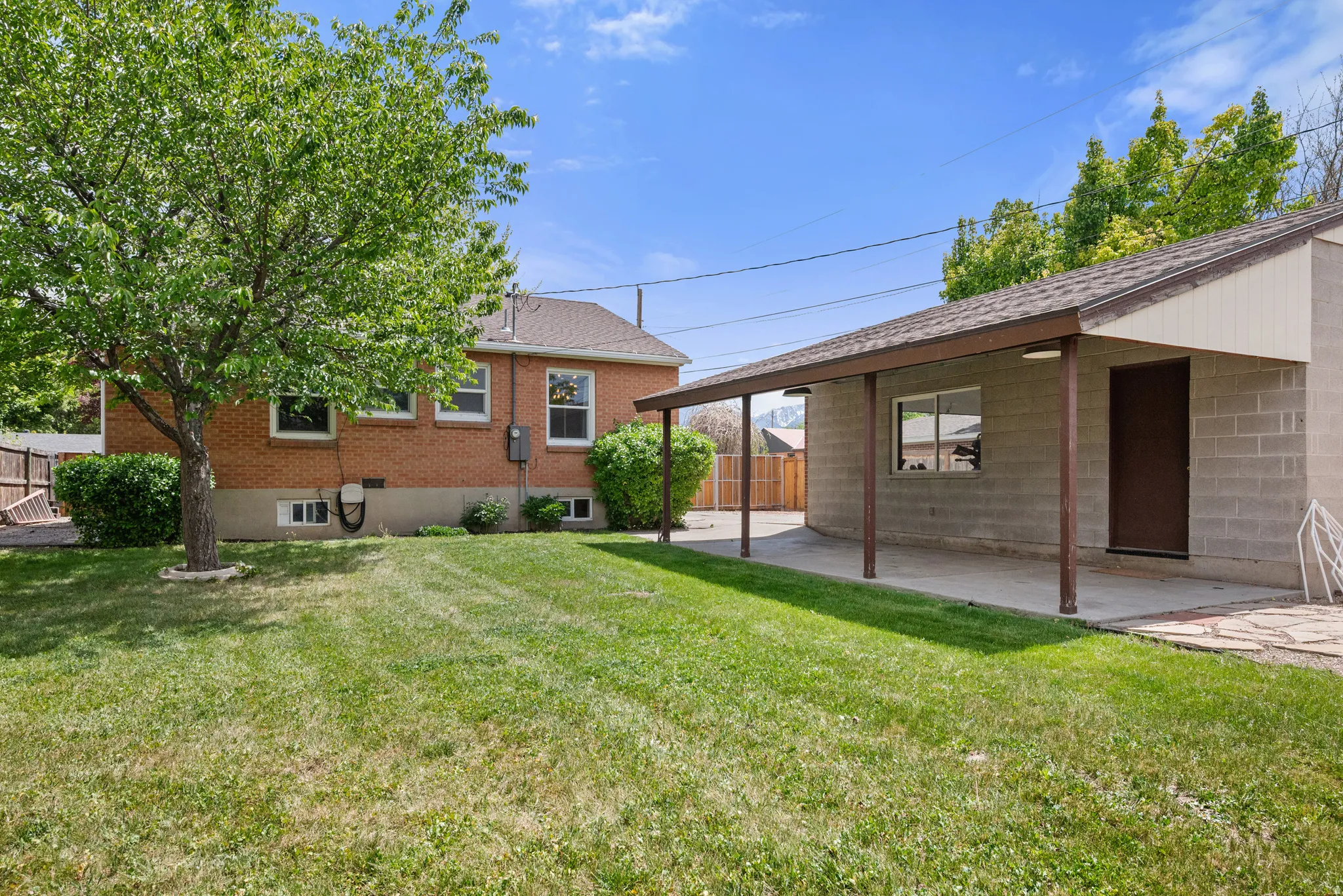 Expansive green lawn featuring a mature shade tree, brick exterior, and a detached structure with a covered patio