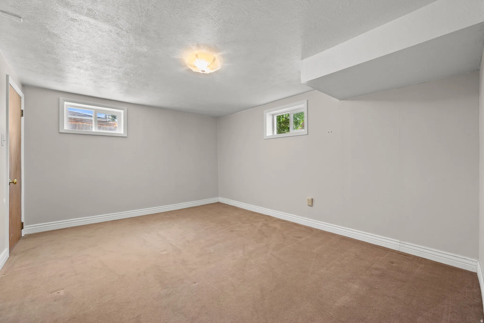 Carpeted interior space featuring neutral wall paint, white trim, a flush-mount ceiling light fixture, and two small windows