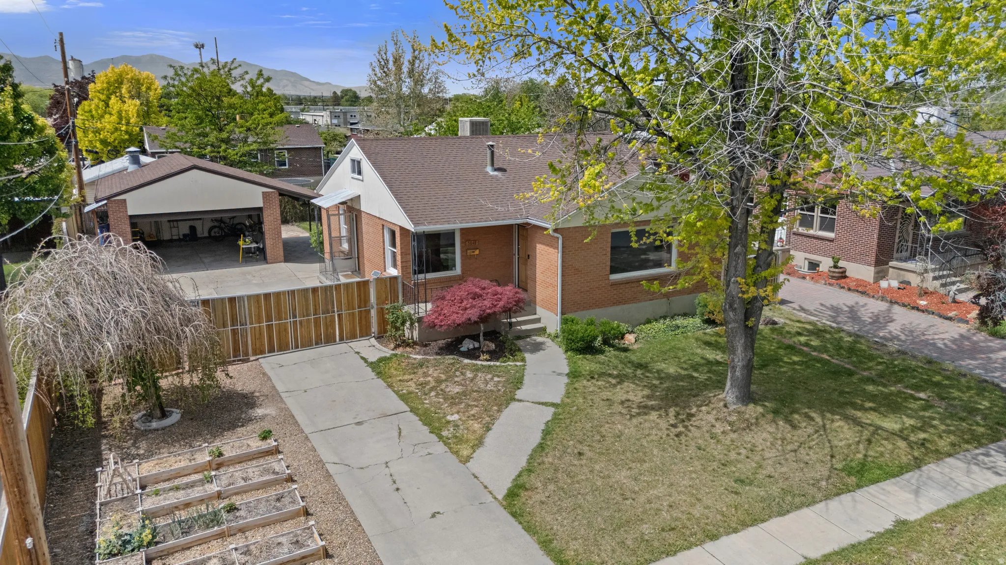 Brick exterior residence with a brown shingle roof, a paved driveway, mature trees, and a covered carport structure