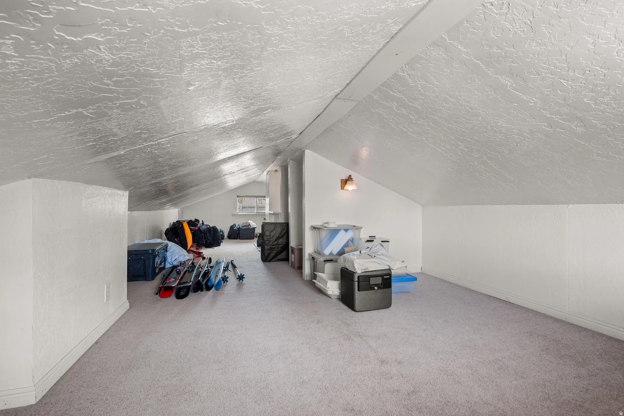 Carpeted attic space featuring sloped ceilings, white painted walls, and a visible window
