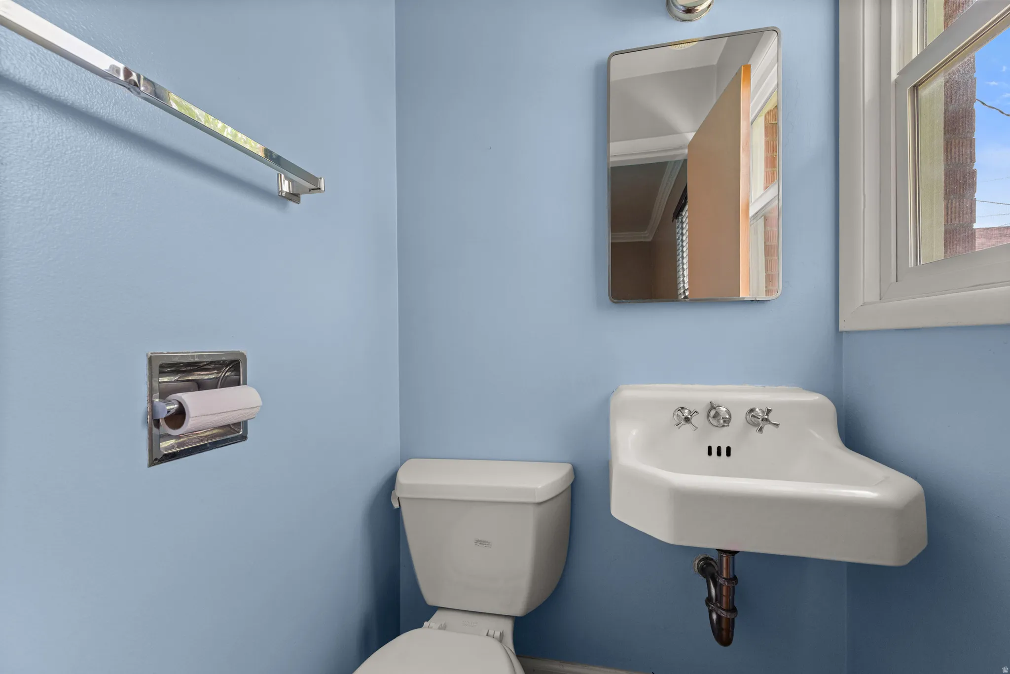 Compact bathroom featuring a wall-mounted porcelain sink with chrome fixtures, a white toilet, and a recessed toilet paper holder