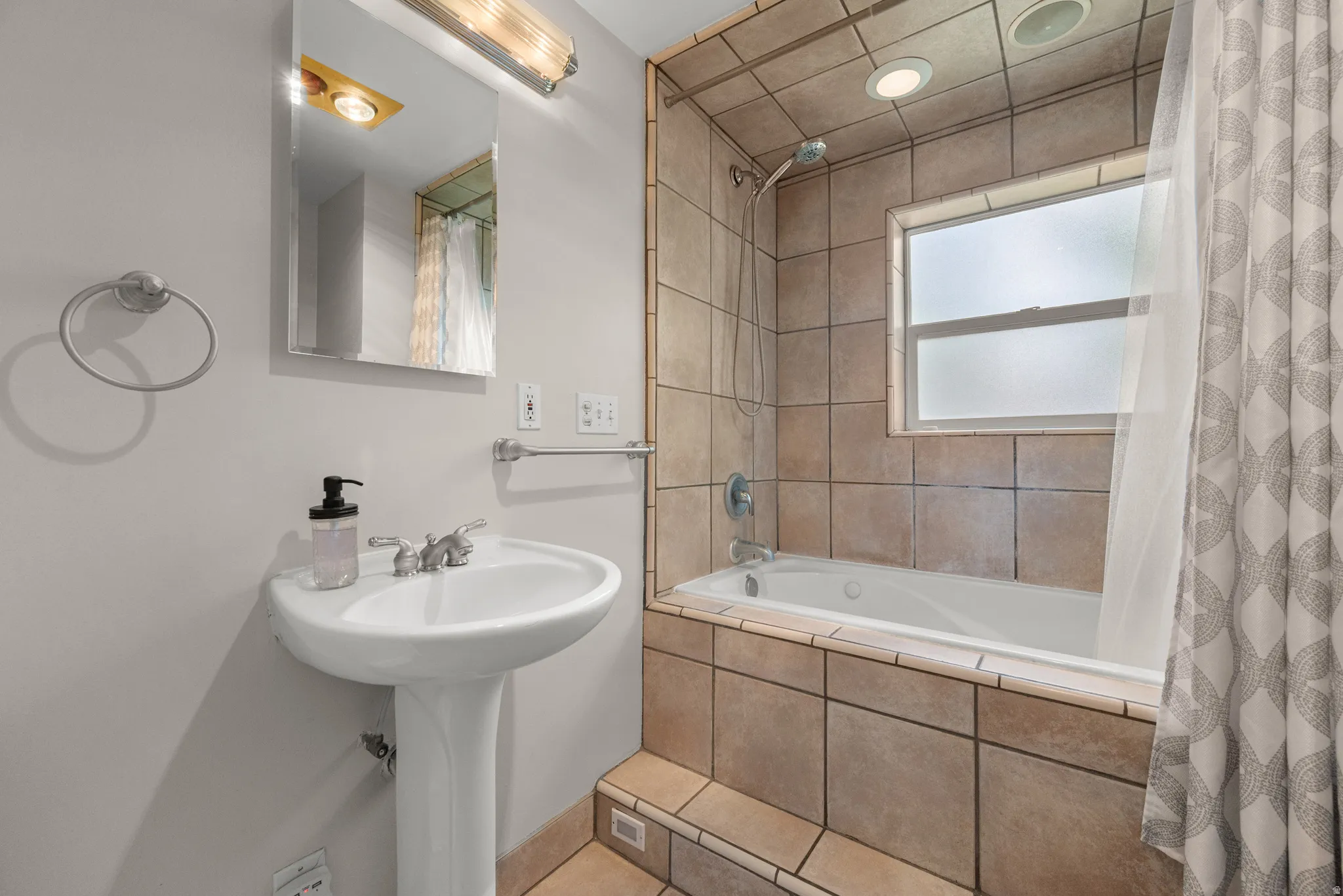 Bathroom featuring a pedestal sink, wall-mounted mirror, and a tiled shower-tub combination
