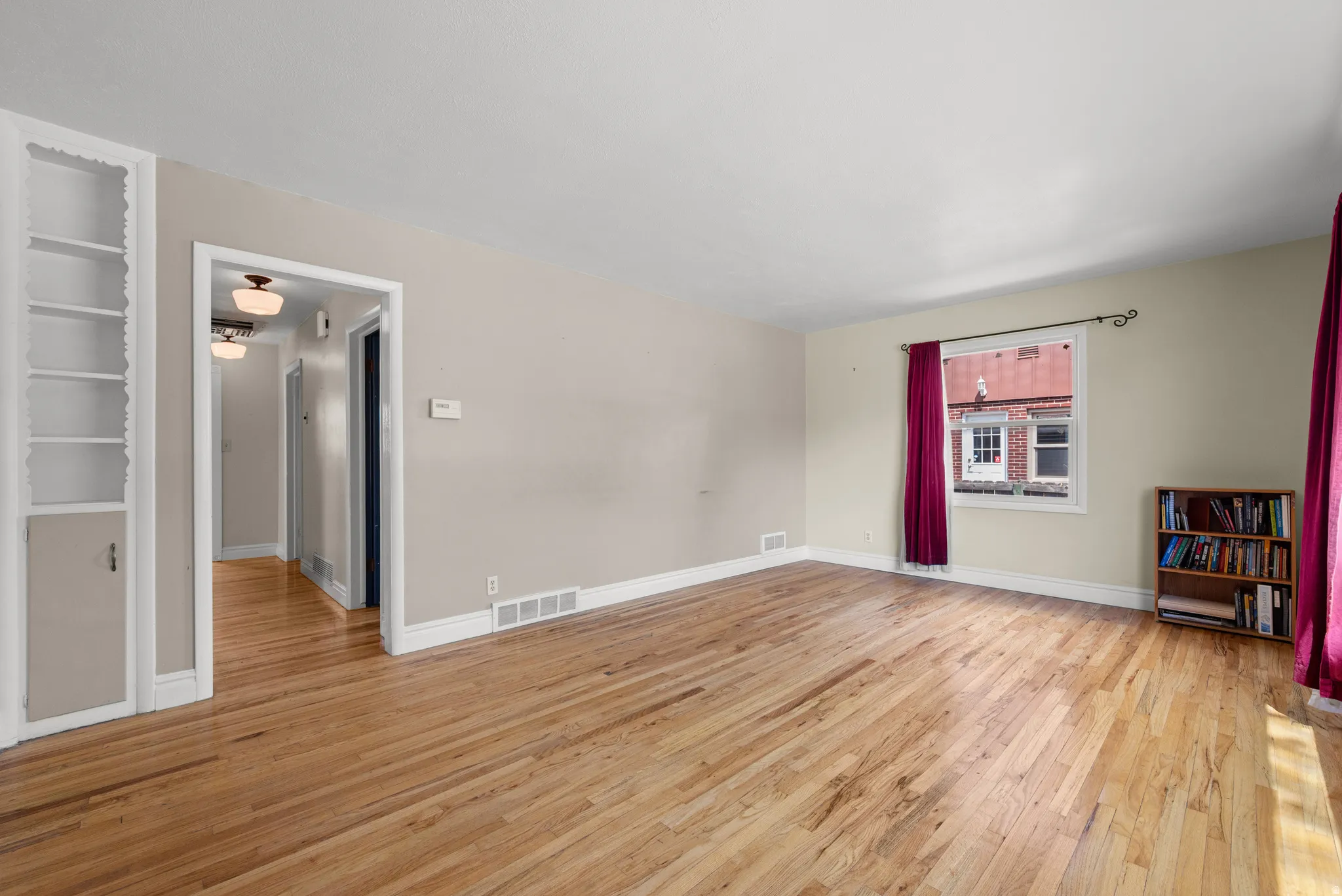 Spacious room featuring wood-finish flooring, white baseboards, and a built-in bookcase with lower cabinetry