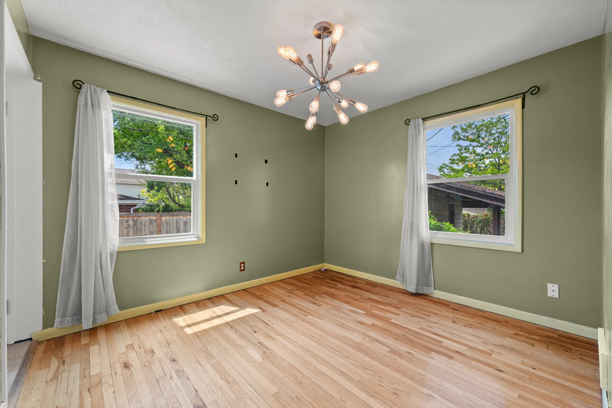 Room featuring light wood-finish flooring, two windows with white trim, and a modern sputnik-style ceiling light fixture
