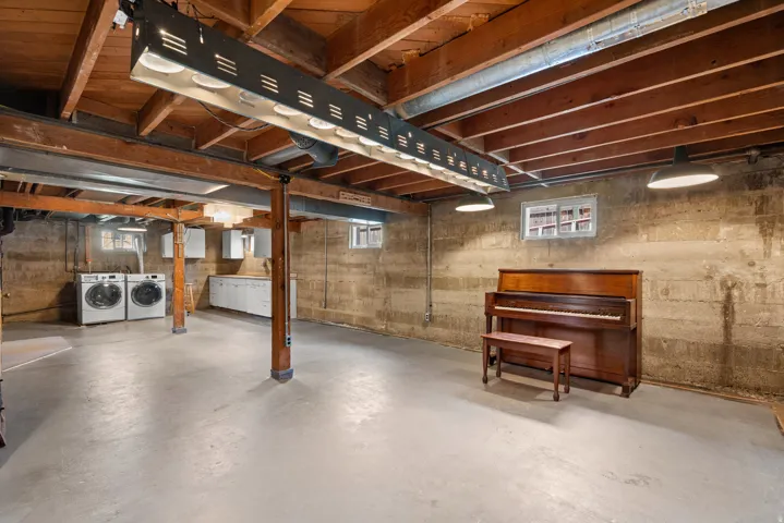 Spacious unfinished basement featuring exposed wood joists, concrete flooring, and multiple utility windows