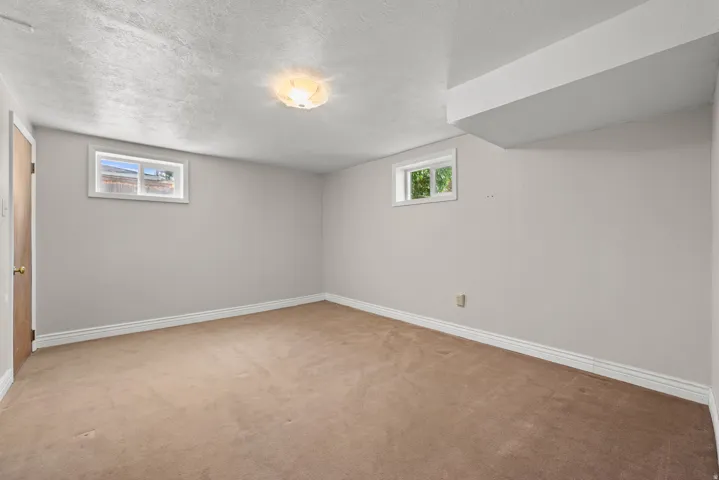 Carpeted interior space featuring neutral wall paint, white trim, a flush-mount ceiling light fixture, and two small windows