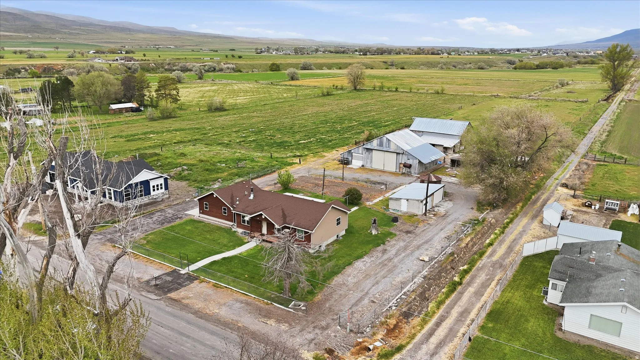 Expansive rural property featuring two residential structures, multiple outbuildings with metal roofs, large open fields, and mountain terrain in the distance