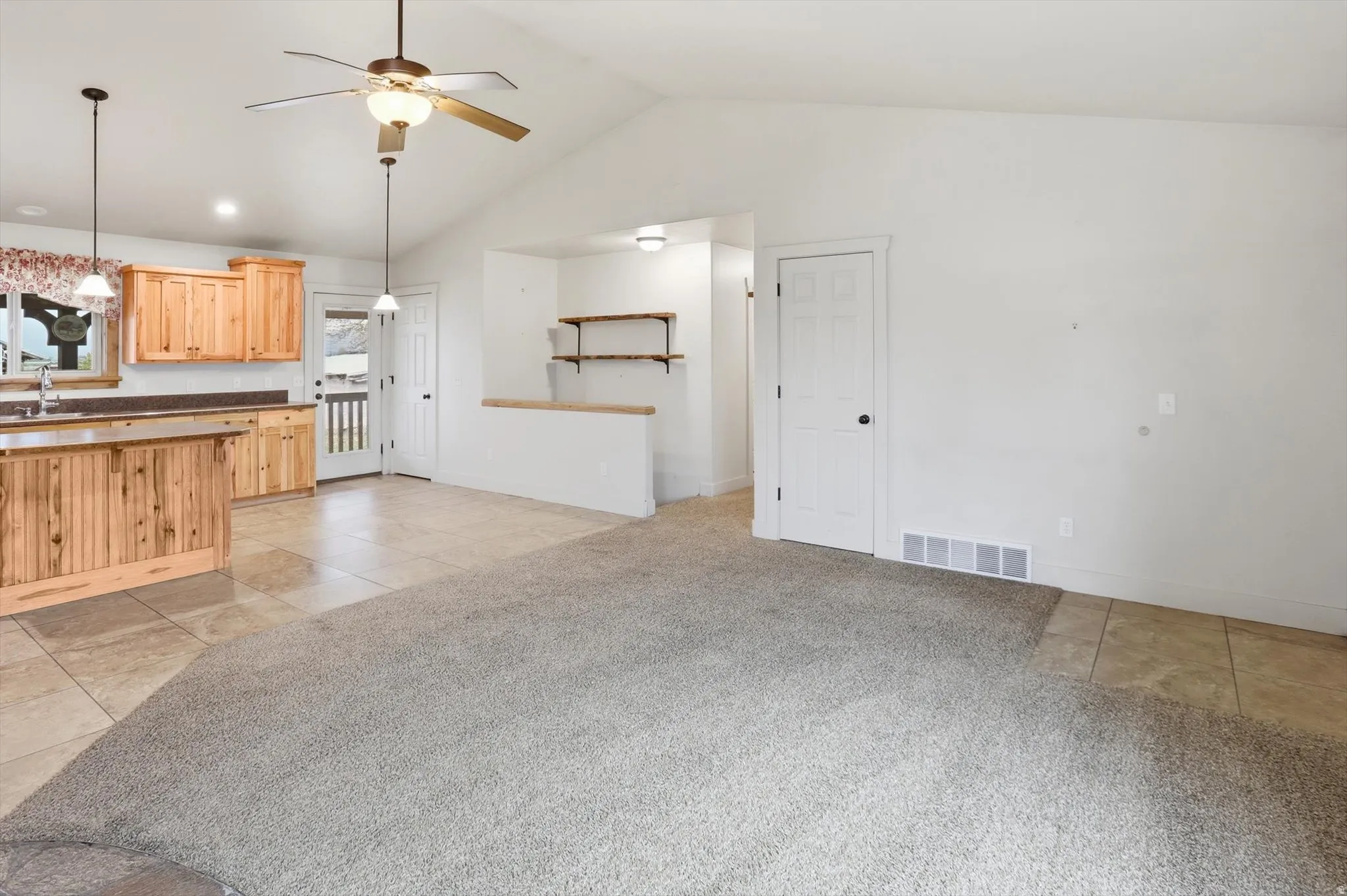 Expansive open-concept living area featuring vaulted ceilings, light wood-finish cabinetry, and a kitchen island with seating
