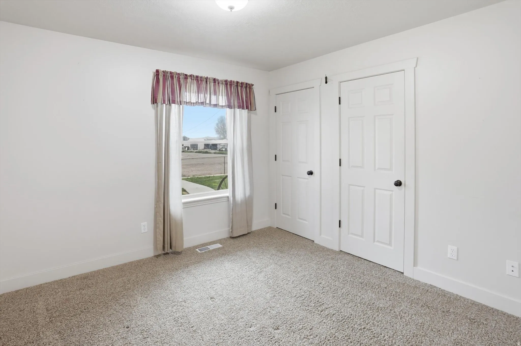 Bright room featuring a window with white trim, two white paneled doors with black hardware, and neutral carpet flooring