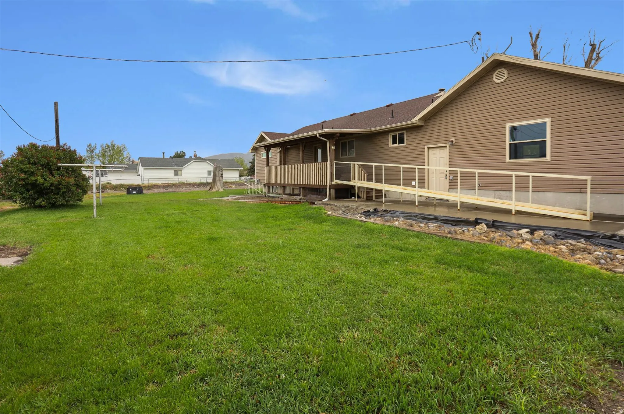 Expansive green lawn with a brown siding exterior, featuring a covered porch, a wooden ramp with railings, and a window with white trim