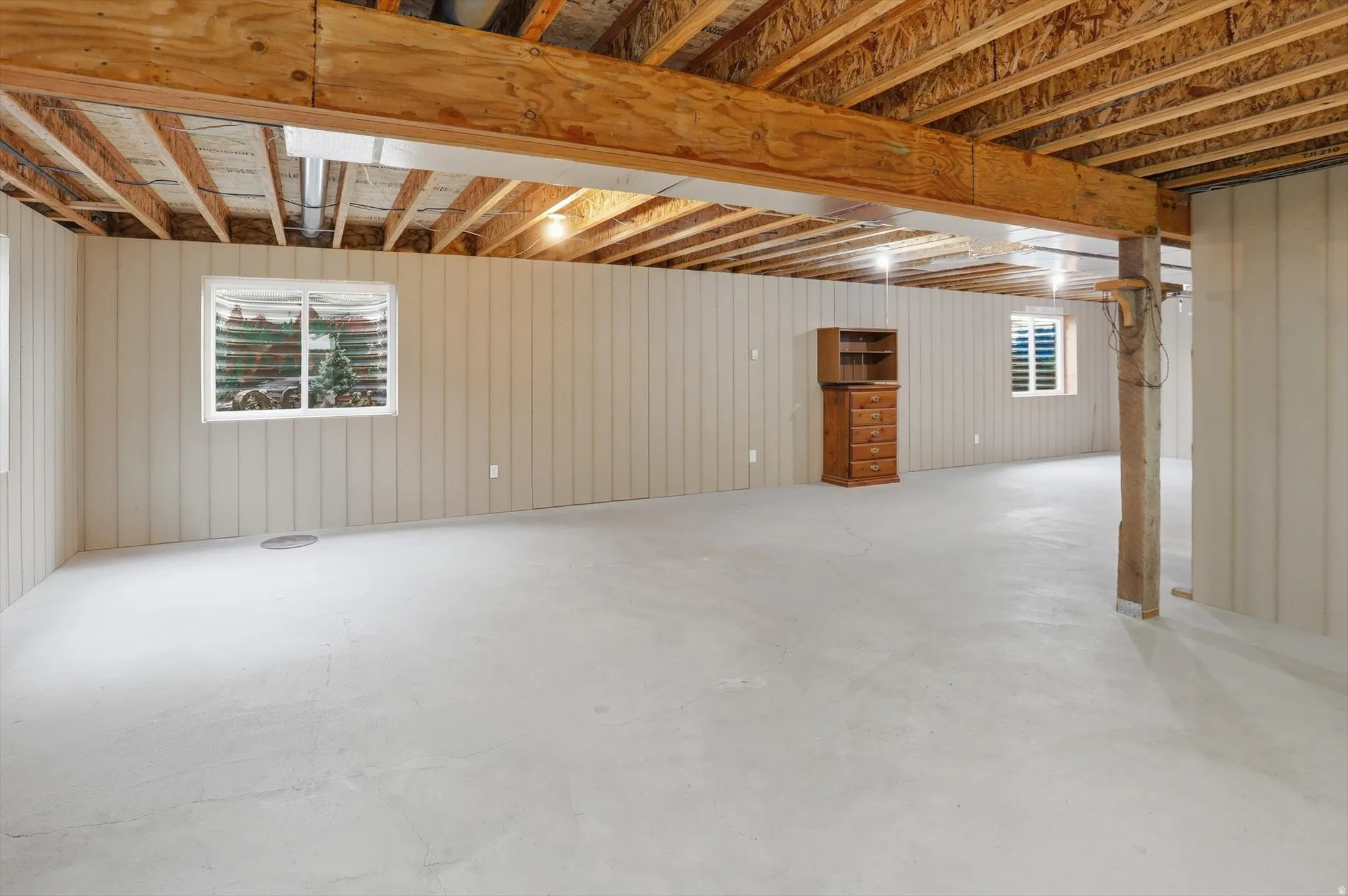Expansive unfinished basement featuring a concrete floor, exposed wood ceiling joists, and vertical paneling on perimeter walls