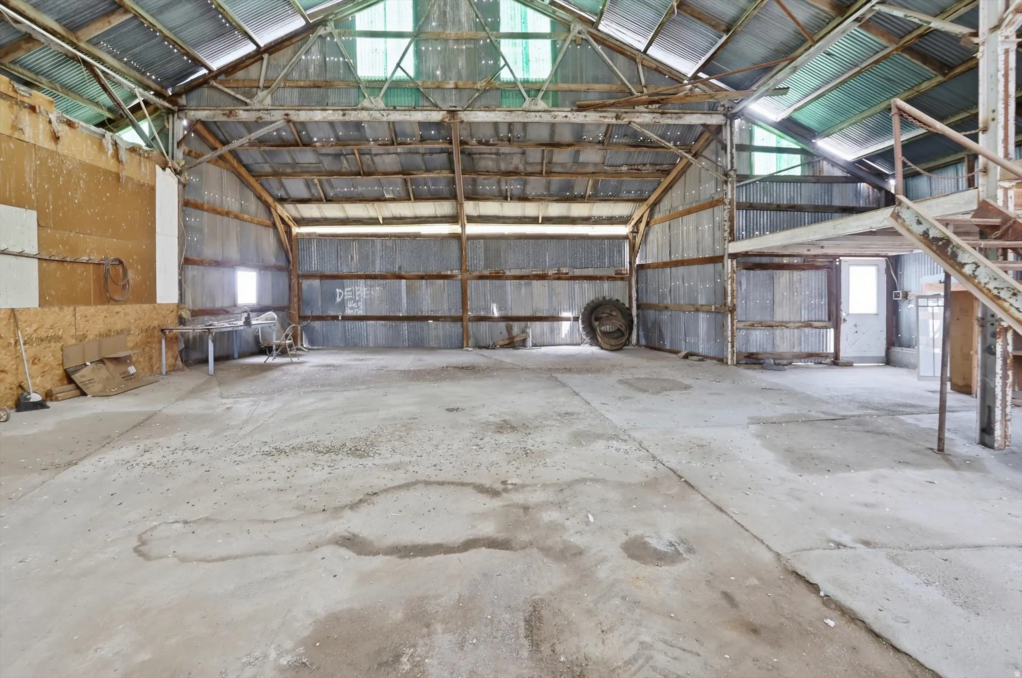 Expansive open-concept interior featuring a high-pitched metal roof, exposed wooden support beams, corrugated metal siding, and a concrete floor