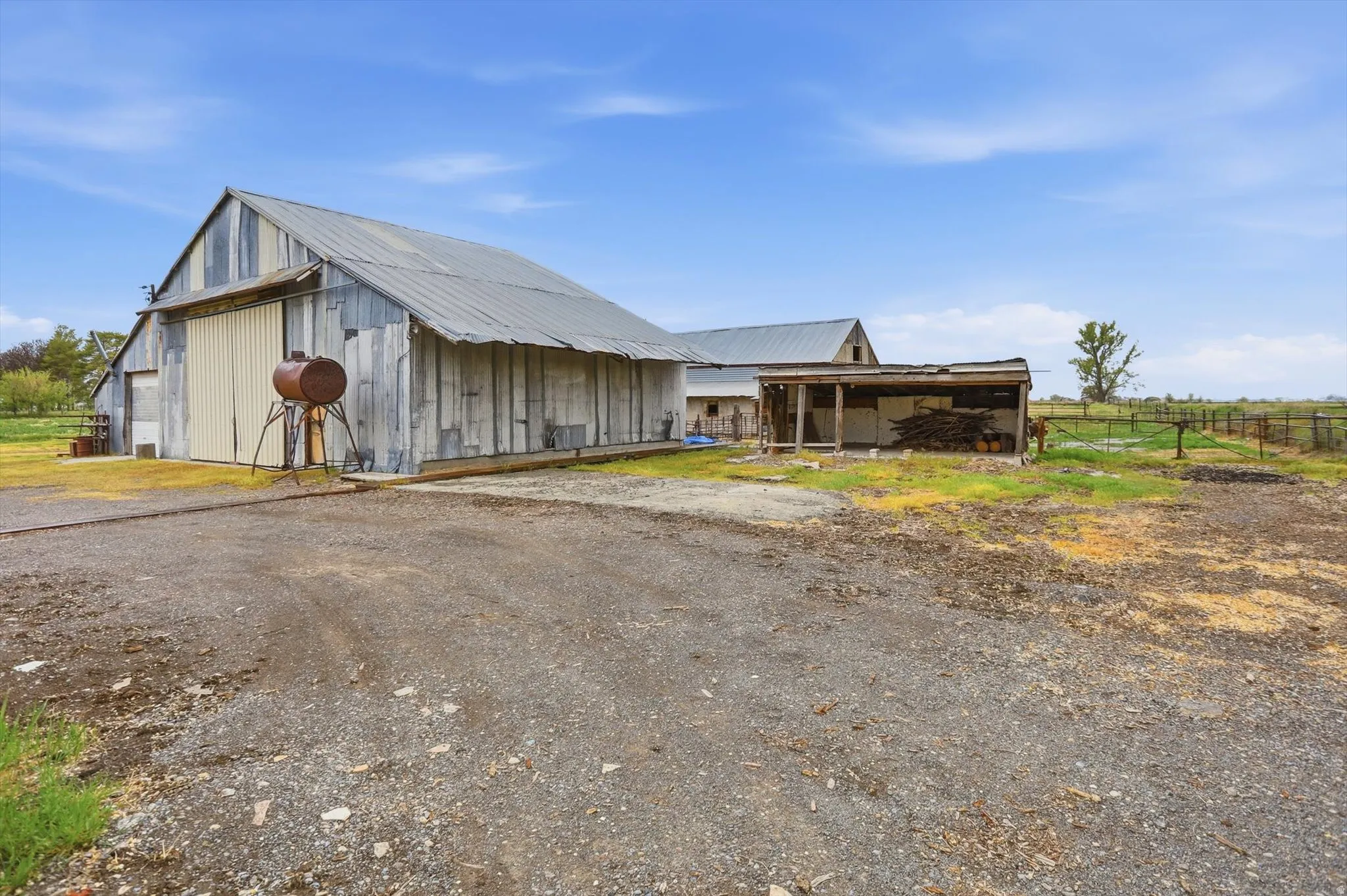 Large utility barn with a corrugated metal roof and siding, expansive gravel drive, and an adjacent open-sided shelter