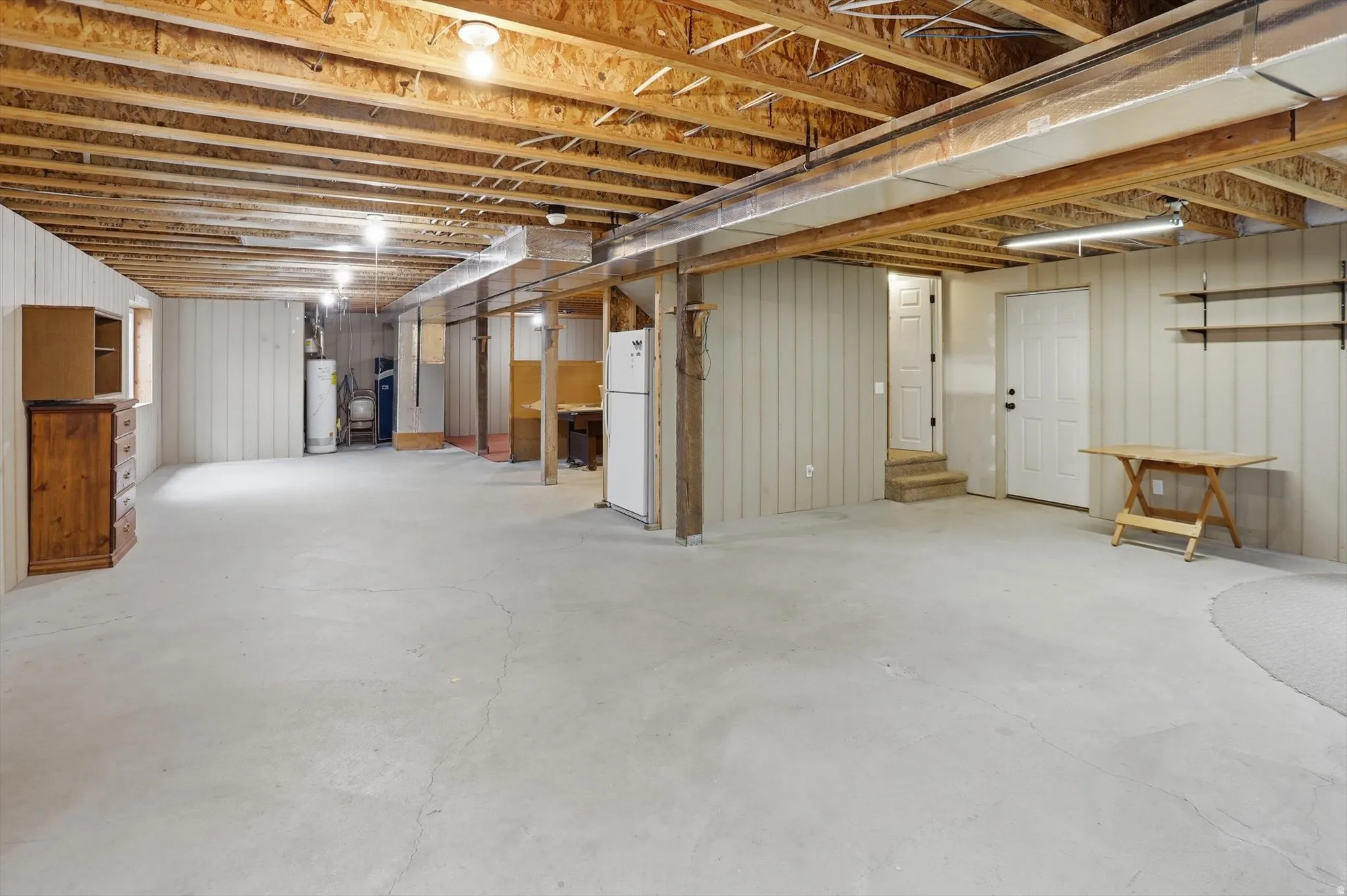 Expansive unfinished basement featuring a concrete floor, exposed wood ceiling joists, and vertical panel walls