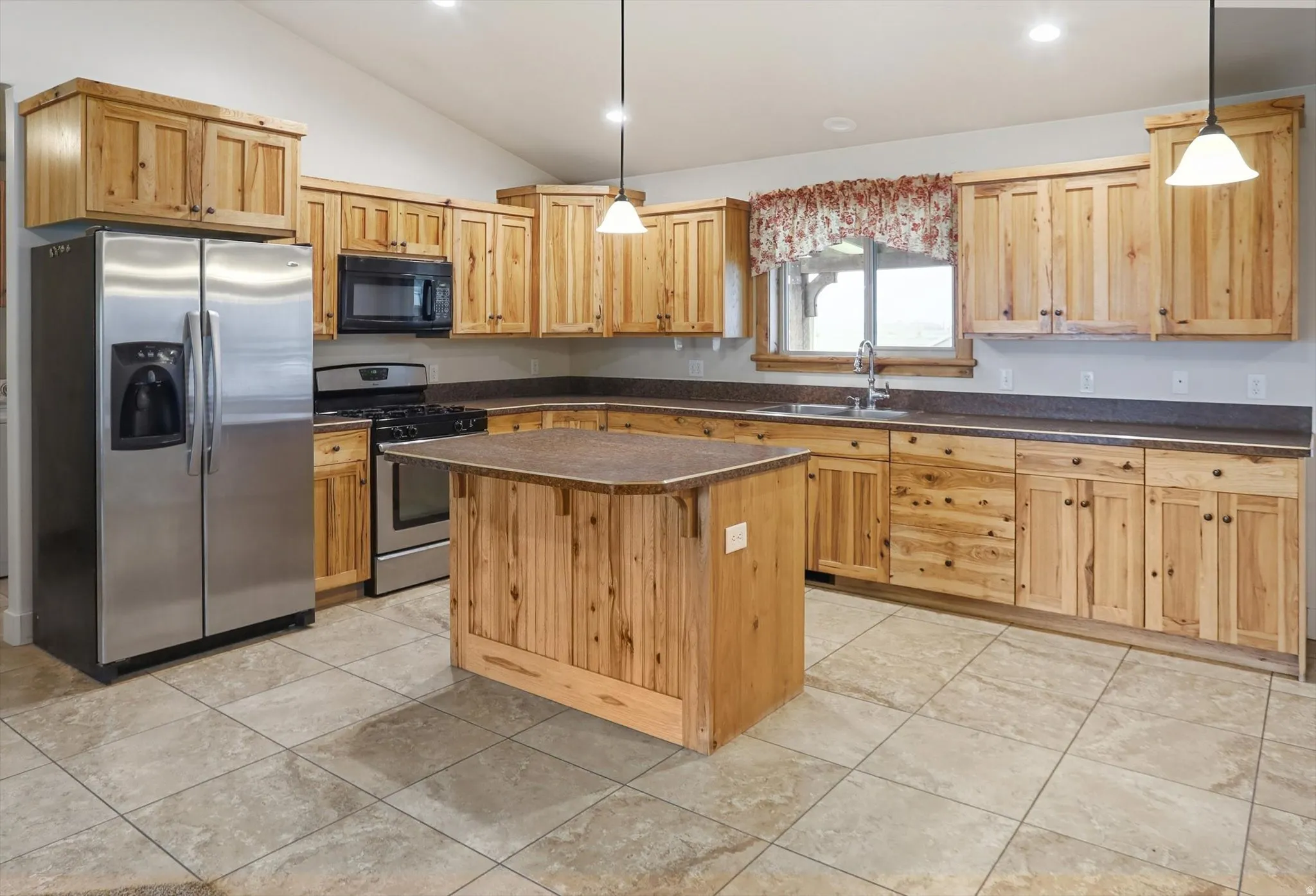 Kitchen featuring extensive wood cabinetry, a central island, stainless steel appliances, and tile flooring