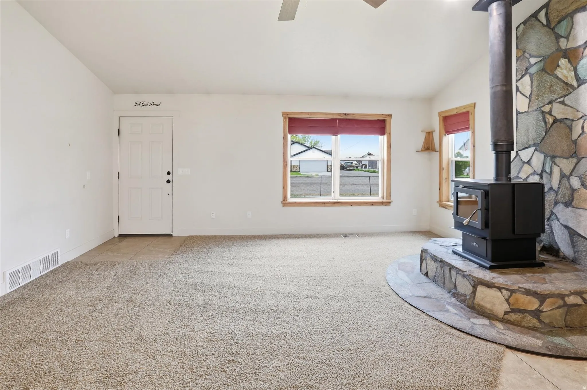 Living area featuring a stone accent wall with a built-in wood-burning stove, two windows with wood trim, and light-colored carpeting