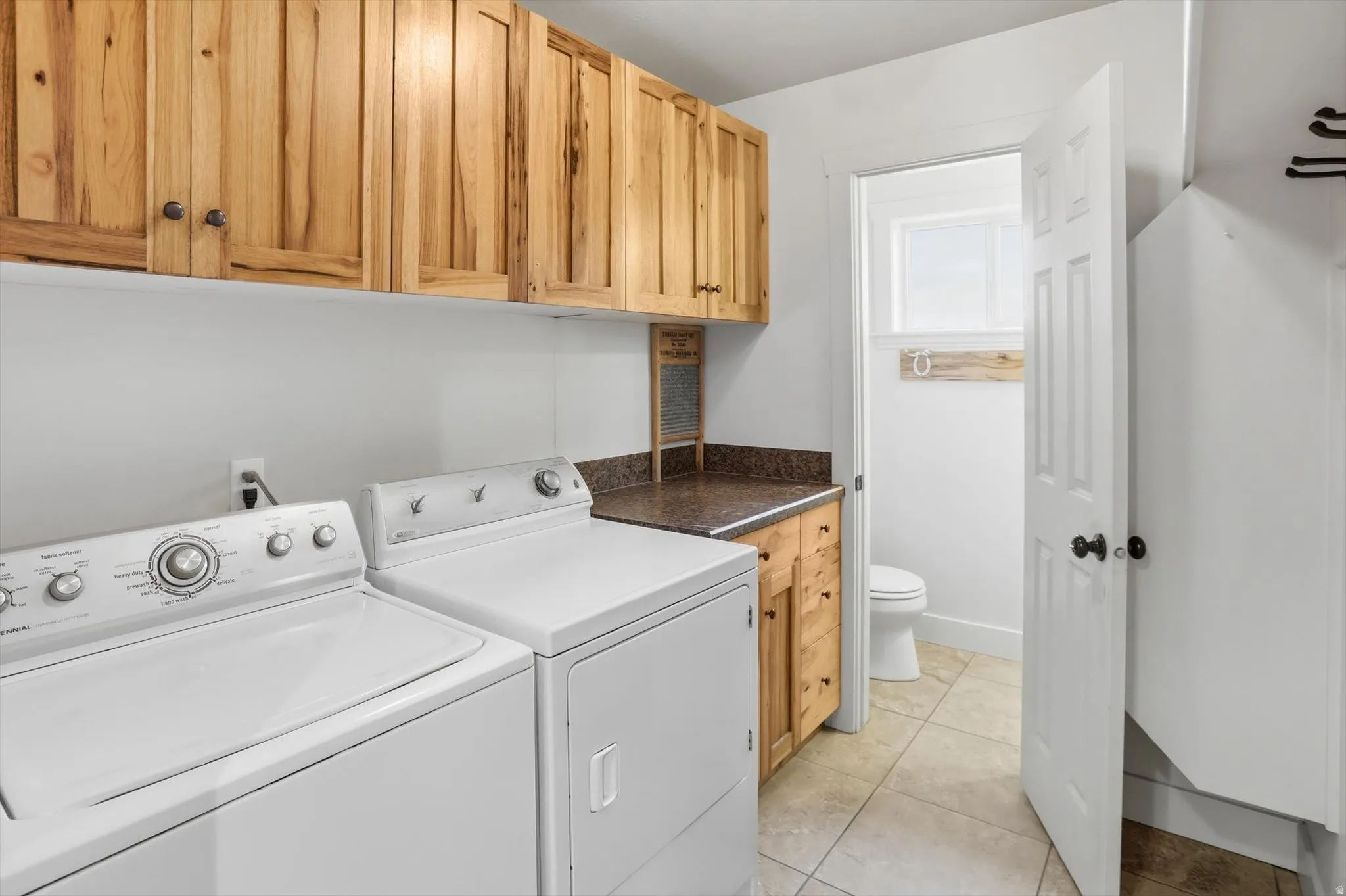Dedicated laundry area with warm wood-finish cabinetry, solid surface countertop, and tile flooring