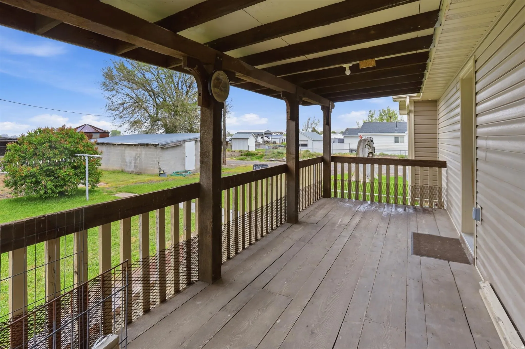 Covered wooden deck with wood railing, siding exterior, and expansive grass yard