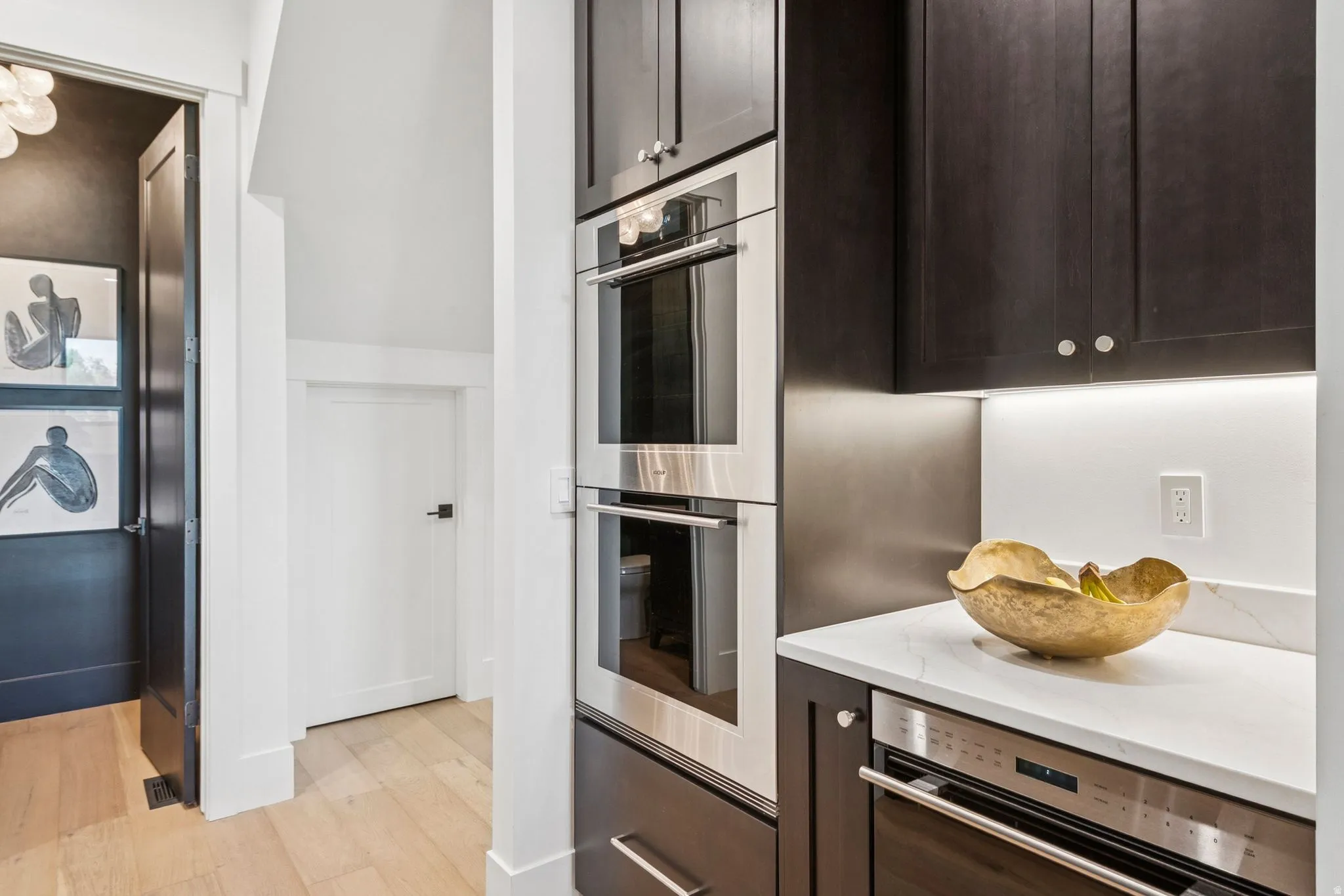 Wolf double ovens and microwave, dark wood-finish cabinetry, and quartz countertops with under-cabinet lighting.