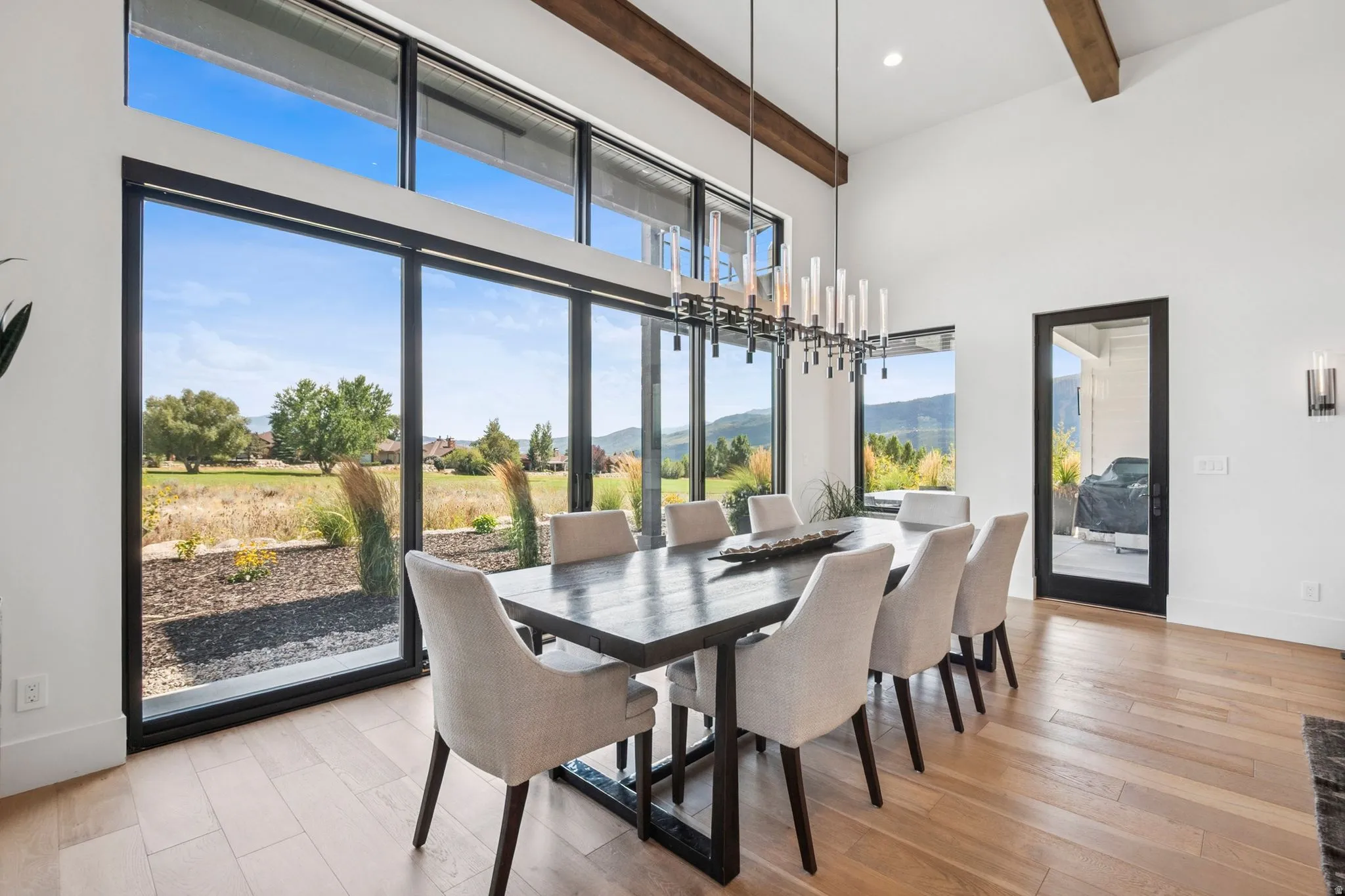 Dining area featuring expansive floor-to-ceiling windows, 14' high ceilings with exposed wood beams, designer lighting, and light hardwood floors.
