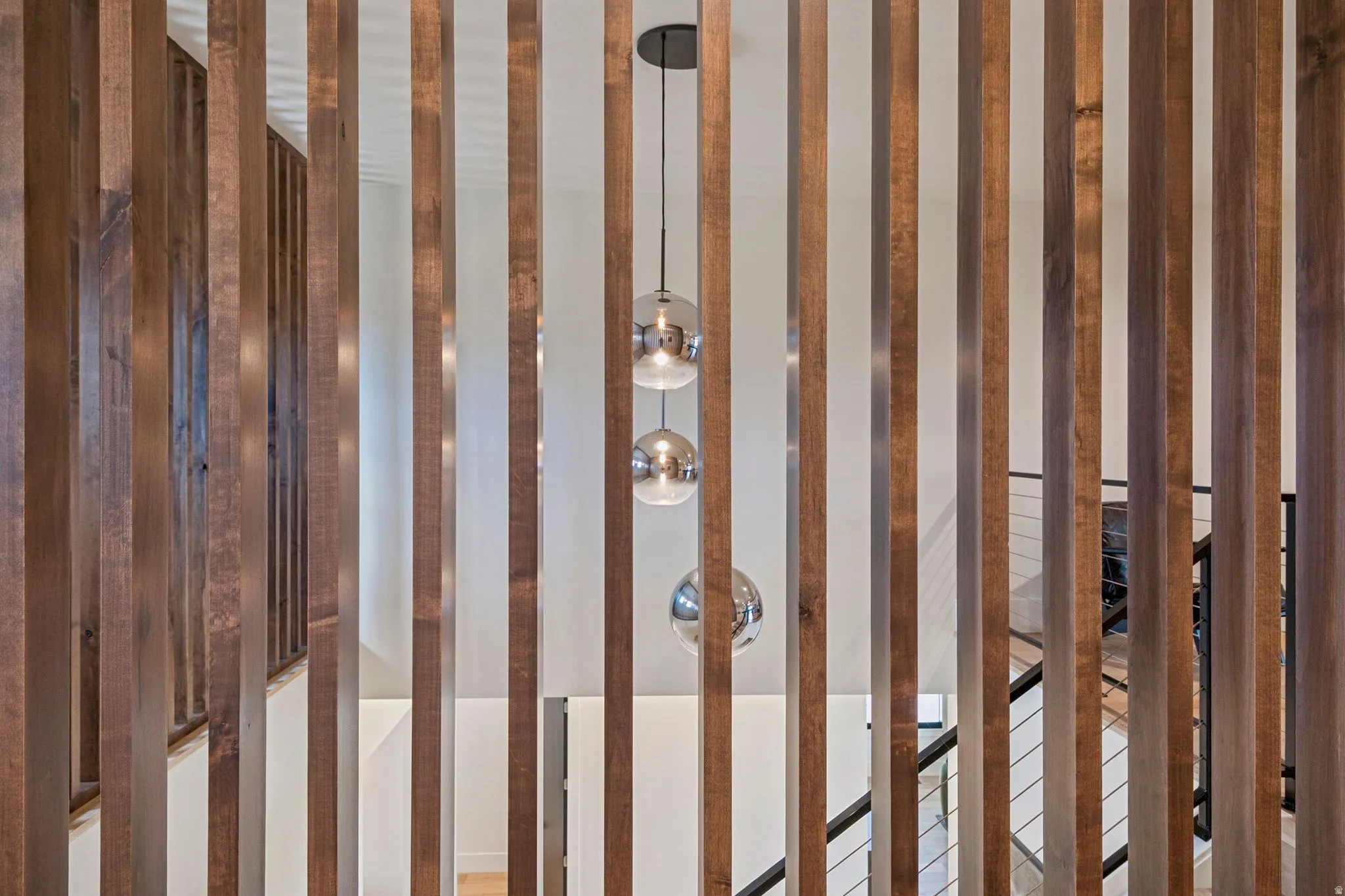 Decorative wood slat screen with a trio of spherical pendant lights and a contemporary staircase featuring black railings and cable infill.