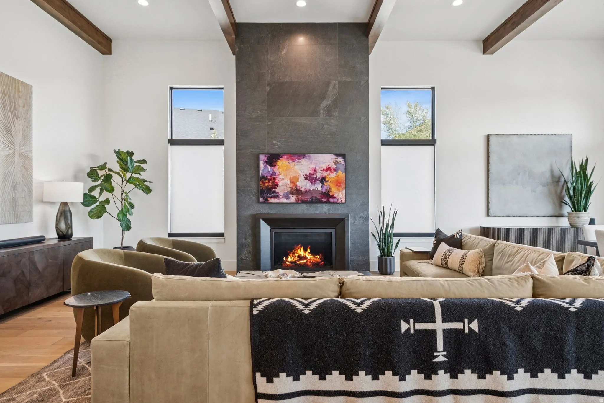 Living area featuring a floor-to-ceiling fireplace with stone-finish surround, high ceilings with exposed wood beams, hardwood flooring, and recessed lighting
