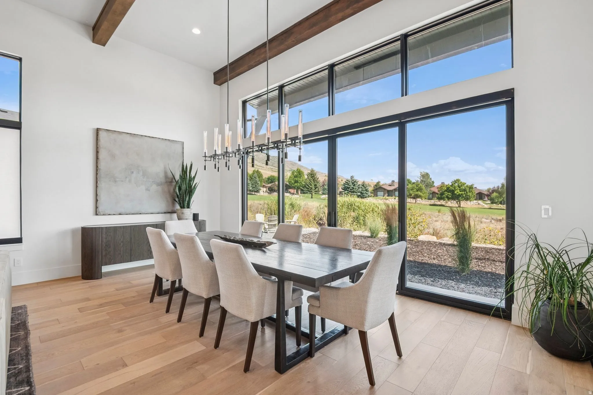 Dining area featuring expansive floor-to-ceiling windows, 14' high ceilings with exposed wood beams, designer lighting, and light hardwood floors.
