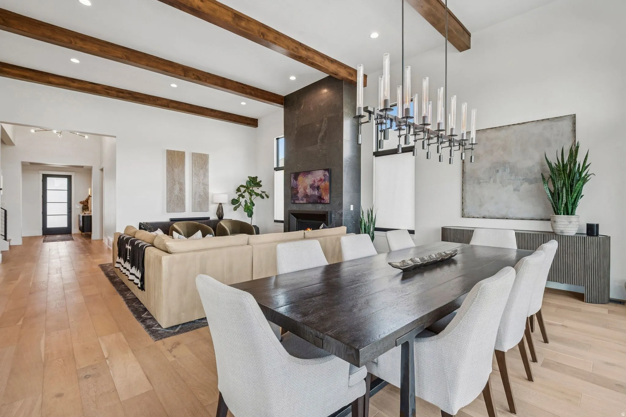 Dining area featuring expansive floor-to-ceiling windows, 14' high ceilings with exposed wood beams, designer lighting, and light hardwood floors.