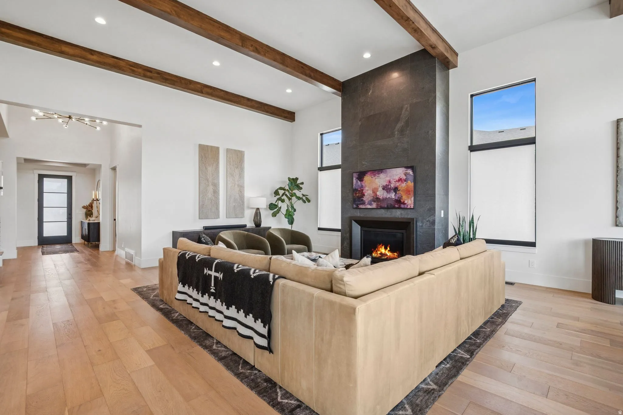 Living area featuring a floor-to-ceiling dark stone fireplace with custom metal hearth, hardwood flooring, 14' high ceilings with exposed wood beams, and tall windows.