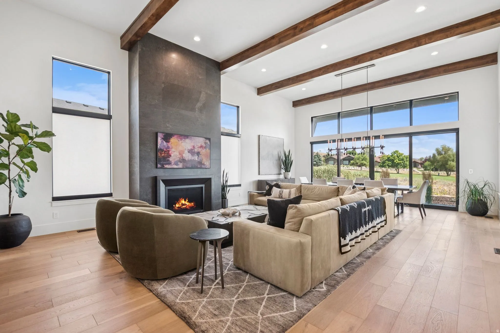 Spacious great room featuring 14' high vaulted ceilings with exposed wood beams, a floor-to-ceiling stone-clad fireplace, and expansive windows offering abundant natural light.