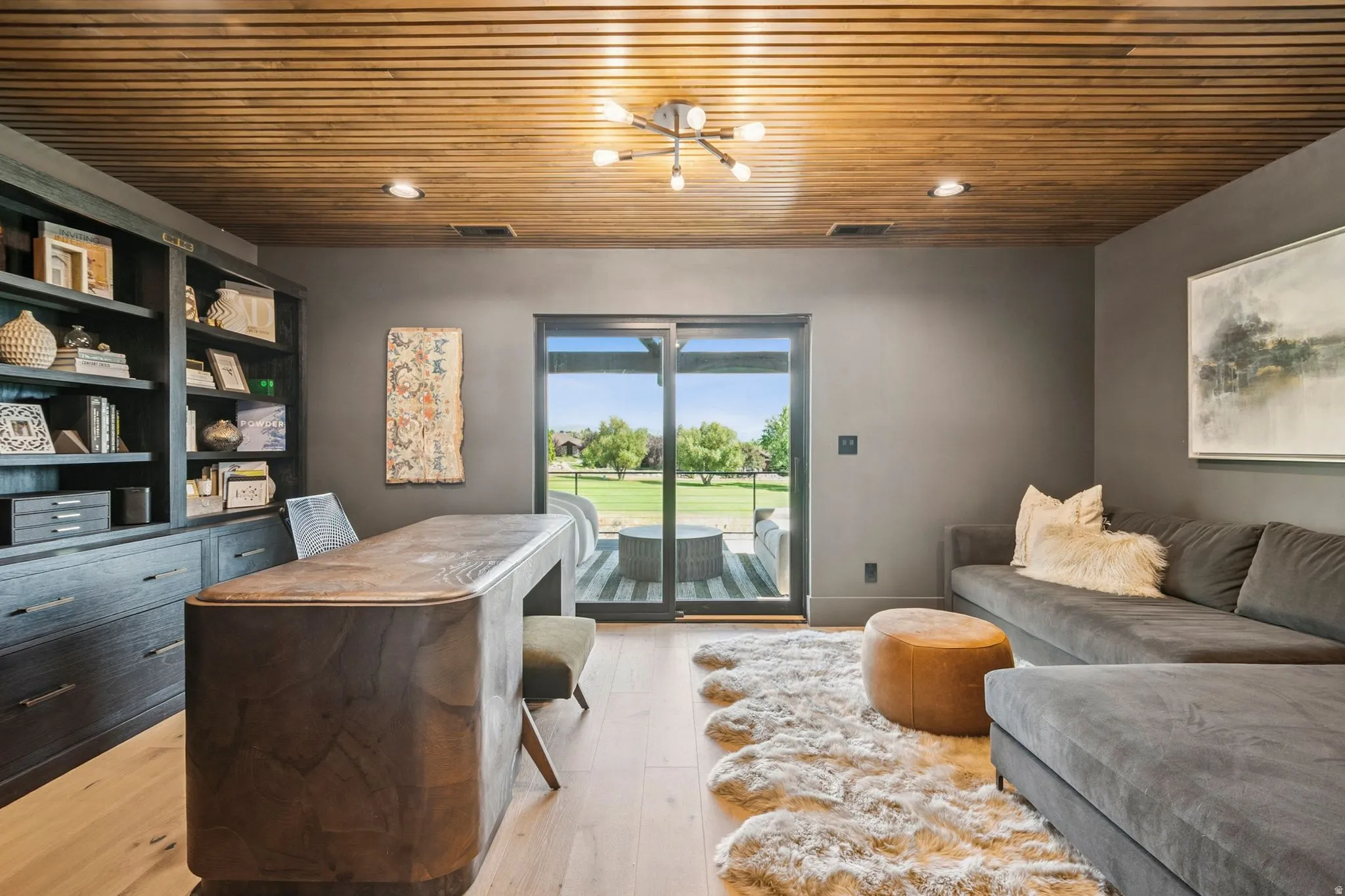 Stunning designer office with slatted wood ceiling, bookcases, and slider that opens to covered deck.