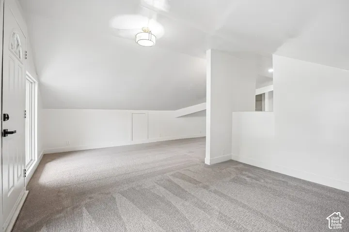 Expansive carpeted area featuring a white door with a window, white walls, and a contemporary flush mount light fixture