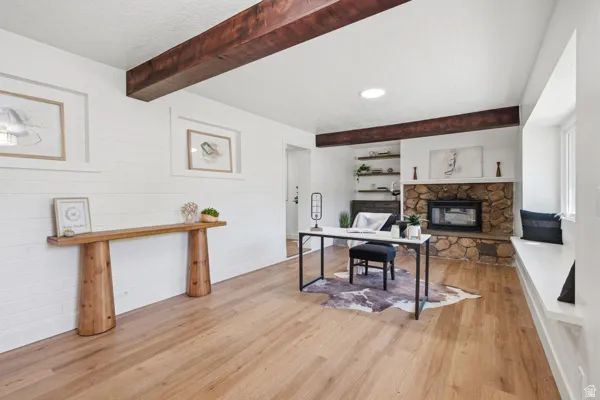Exposed wood ceiling beams, shiplap wall paneling, a stone fireplace with built-in shelving, wood-finish flooring, and a built-in window bench