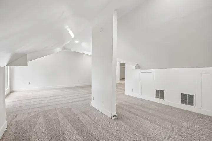 Spacious attic space featuring sloped ceilings, recessed lighting, neutral-toned carpet, built-in access panels, and baseboard trim