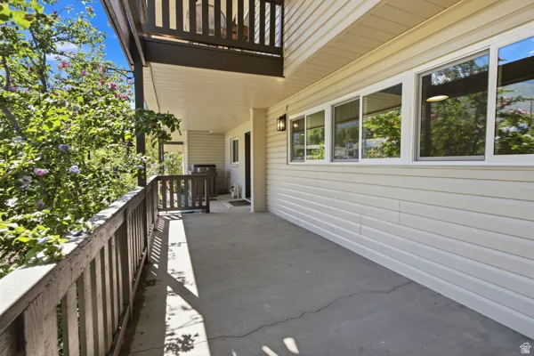 Expansive concrete patio with a dark wood railing, overhead balcony, and exterior wall sconce