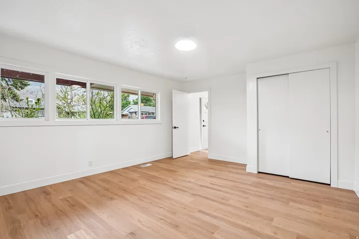 Spacious room featuring wood-finish flooring, white walls, and bright overhead lighting
