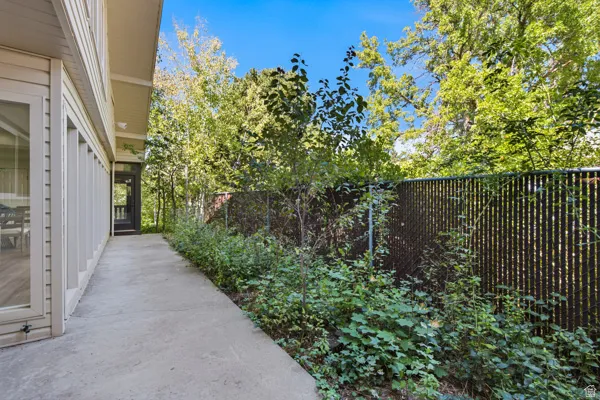 Exterior siding with multiple windows, concrete walkway, screened porch, chain-link fencing, and mature trees