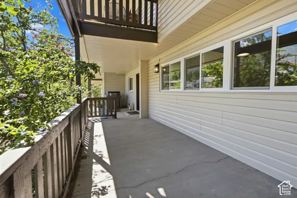 Expansive concrete patio with a dark wood railing, overhead balcony, and exterior wall sconce