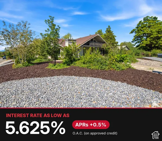 Exterior featuring a gable-roofed residence with a second-story balcony, masonry chimney, and low-maintenance landscaping consisting of gravel ground cover and organic mulch