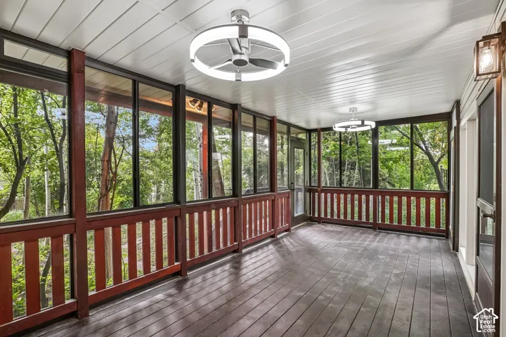 Expansive screened porch featuring dark wood-finish flooring, white paneled ceiling, two contemporary ceiling fans with integrated lighting, a wall-mounted exterior lantern, and full-height screens with wood railing
