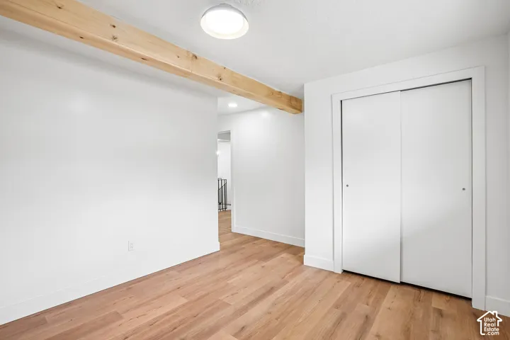Room featuring wood-finish flooring, a prominent exposed wood beam, white walls, and a ceiling-mounted light fixture