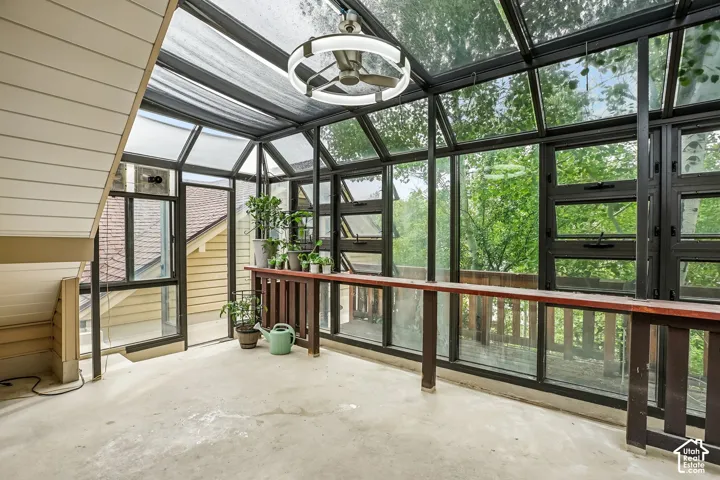 Sunroom featuring a full glass ceiling, expansive windows, a ceiling fan fixture, and a built-in wooden counter with a railing