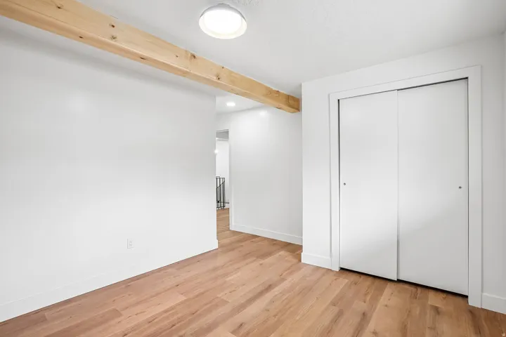 Room featuring wood-finish flooring, a prominent exposed wood beam, white walls, and a ceiling-mounted light fixture