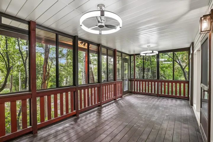 Expansive screened porch featuring dark wood-finish flooring, white paneled ceiling, two contemporary ceiling fans with integrated lighting, a wall-mounted exterior lantern, and full-height screens with wood railing