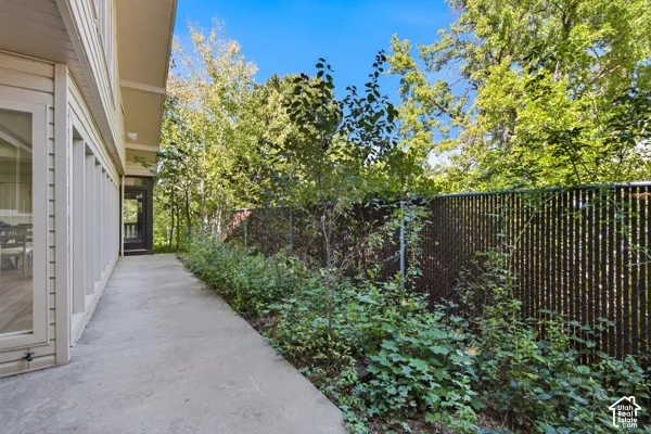 Exterior siding with multiple windows, concrete walkway, screened porch, chain-link fencing, and mature trees