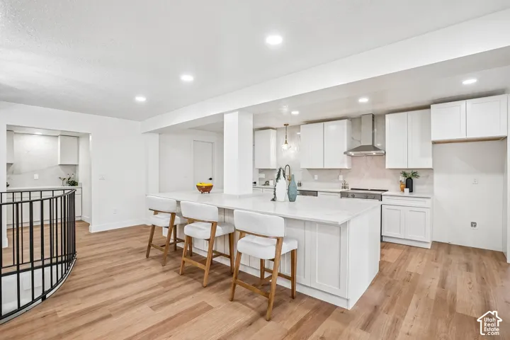 Modern kitchen featuring a large central island with seating, white shaker cabinetry, stainless steel appliances, and wood-finish flooring