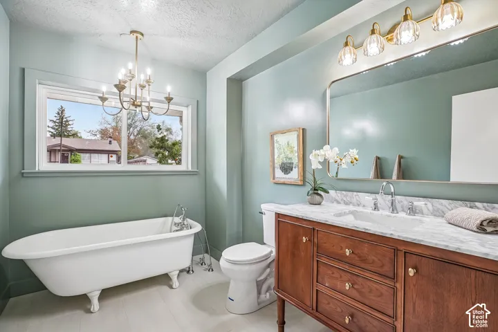 Bathroom featuring a white clawfoot bathtub with chrome fixtures, a wood-finish vanity with a white marble-patterned countertop and an integrated sink, a rectangular mirror with a gold-tone frame, and a gold-tone light fixture with fluted glass shades