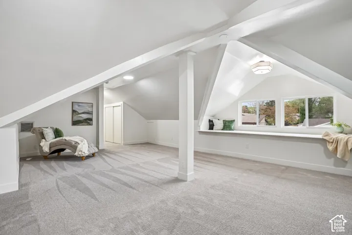 Expansive carpeted room featuring sloped ceilings, white painted walls, and white trim