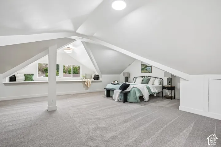 Spacious attic room with light gray carpeting and sloped white ceilings